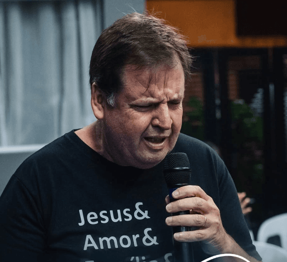 Pastor Walter Friedrich Vogt ministrando com microfone, camiseta com mensagem Jesus e família